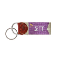 Navy needlepoint key fob with the Sigma Pi Greek letters in gold and white, brown leather trim, and a metal key ring.