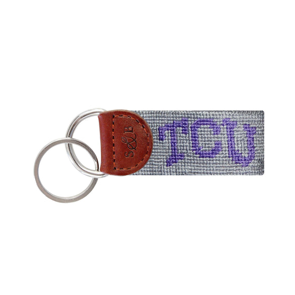Gray needlepoint key fob with the purple TCU “Frog” logo, brown leather trim, and a metal key ring.