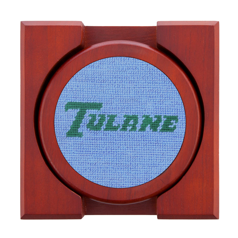 Set of four round wooden coasters with stitched needlepoint logos stacked neatly in a wooden holder.