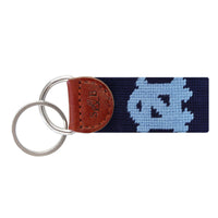Carolina blue needlepoint key fob with the white UNC “NC” logo, brown leather trim, and a metal key ring.