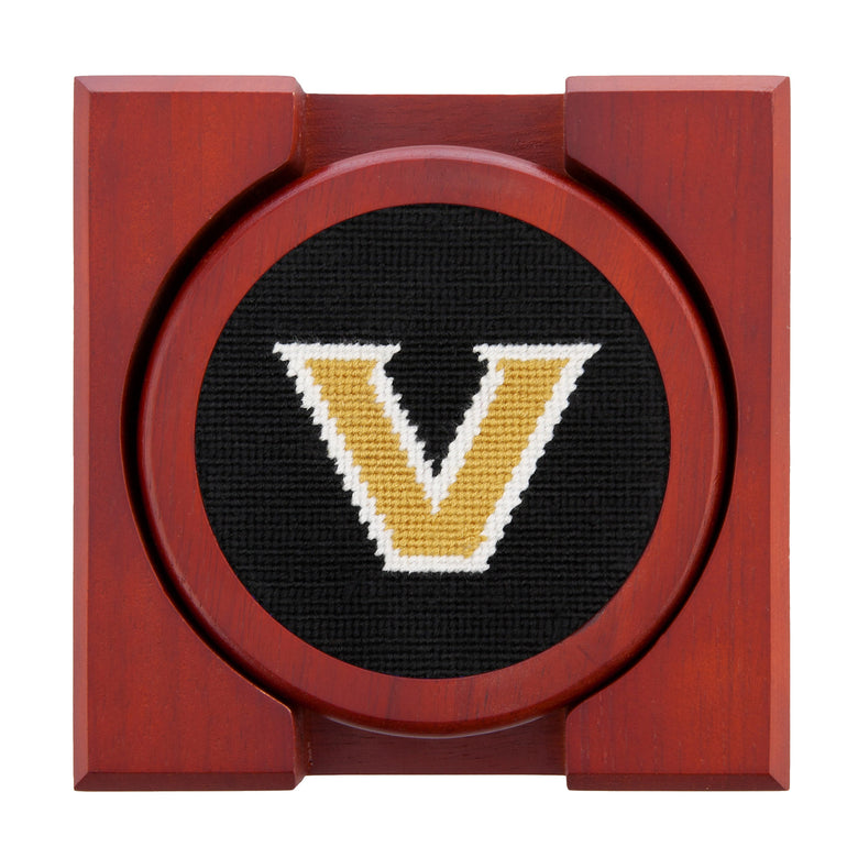 Set of four round wooden coasters with stitched needlepoint logos stacked neatly in a wooden holder.